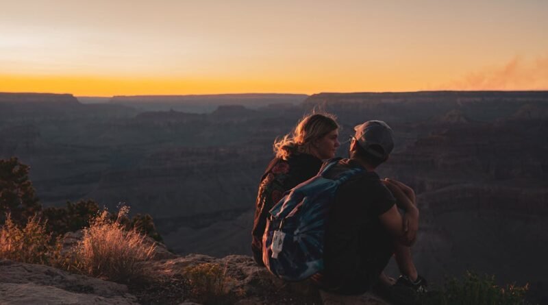 A couple sits on the Grand Canyon edge during sunset, capturing a serene moment of natural beauty.